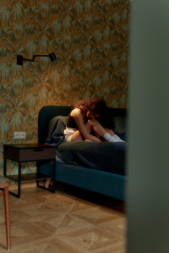 A woman sitting on a bed in a stylish room, reflecting emotions of solitude and introspection.